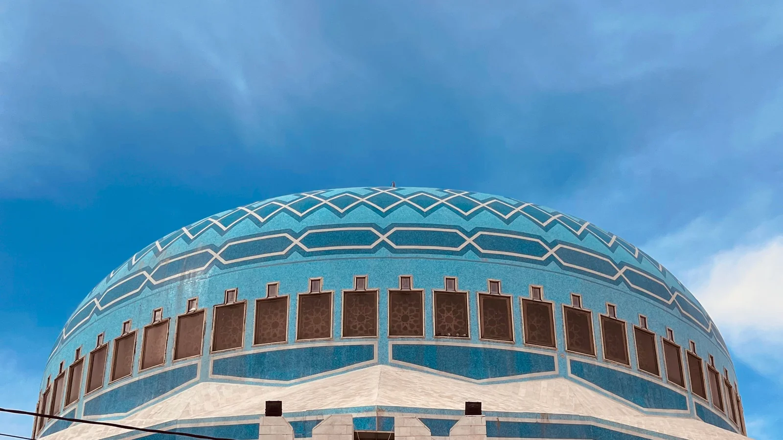 The blue dome and geometric bands of King Abdullah I Mosque in Amman beneath a cloudy sky.