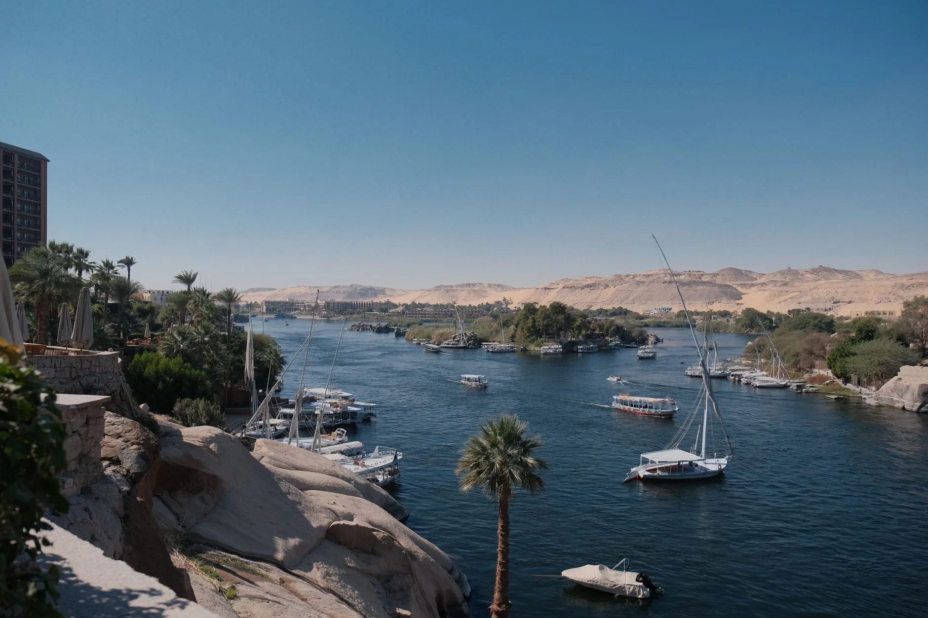 The Nile at Aswan with granite banks, island palms and feluccas beneath a clear sky