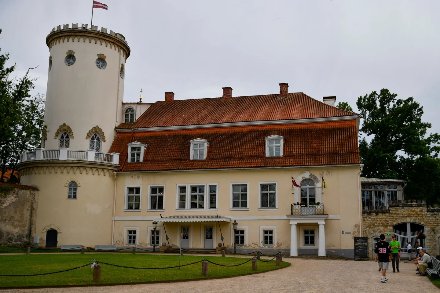 The white round tower and red roofs of Cēsis New Castle beside its lawn