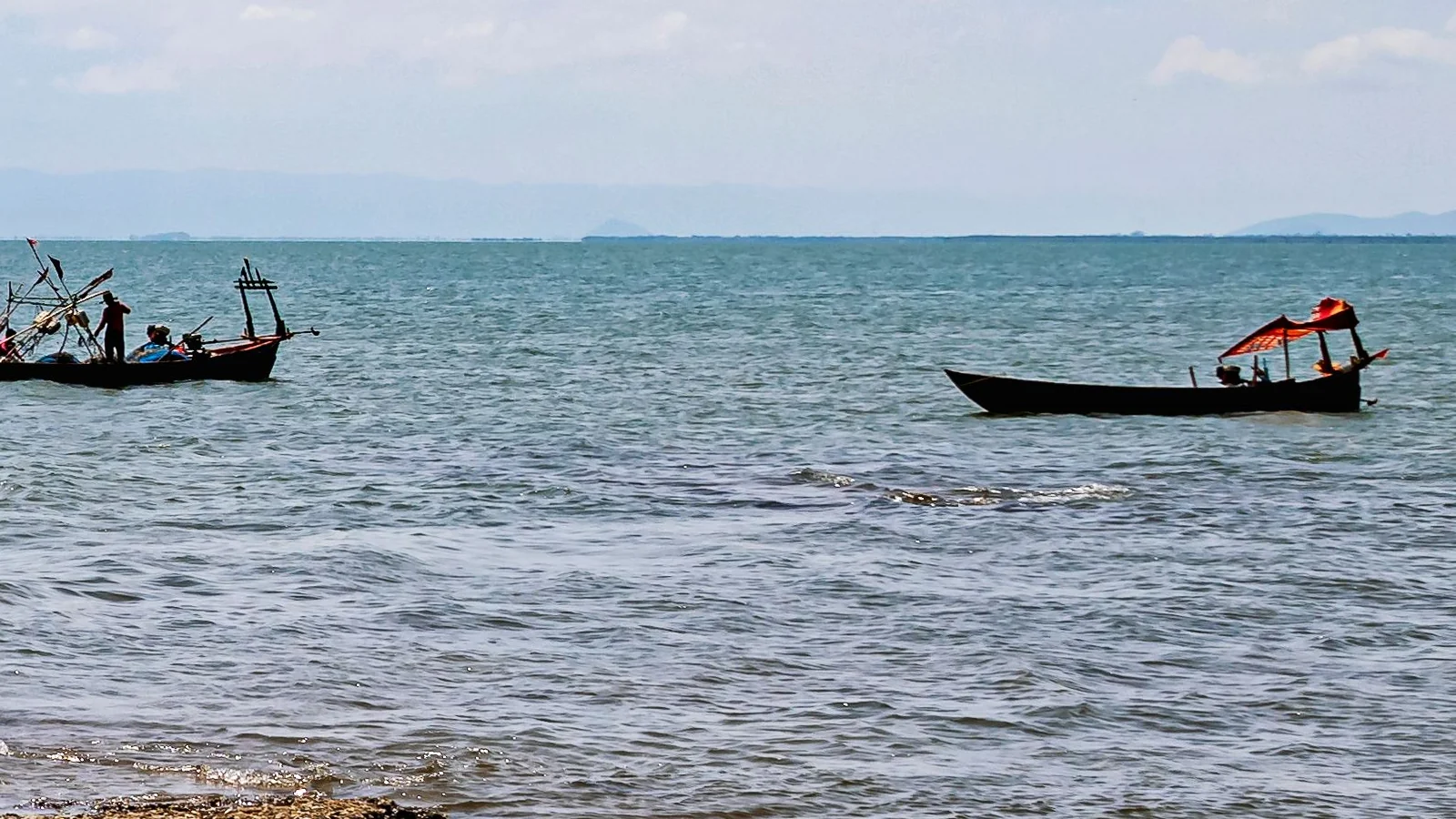 Fishing boats on Kep’s coastal waters, with a low island horizon behind them.