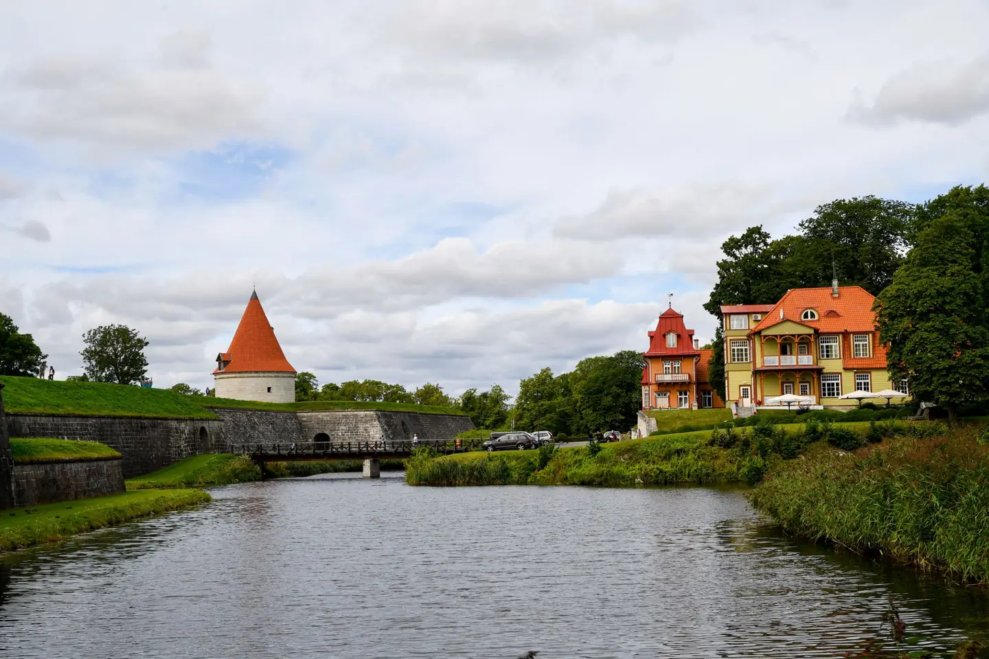 Kuressaare’s castle moat, stone crossing and outer tower, with historic buildings along the park edge