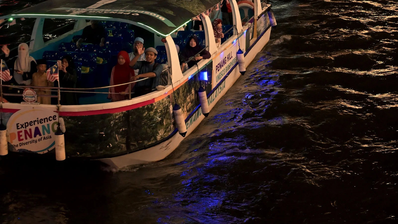 Illuminated sightseeing boats carrying passengers on the Melaka River at night.