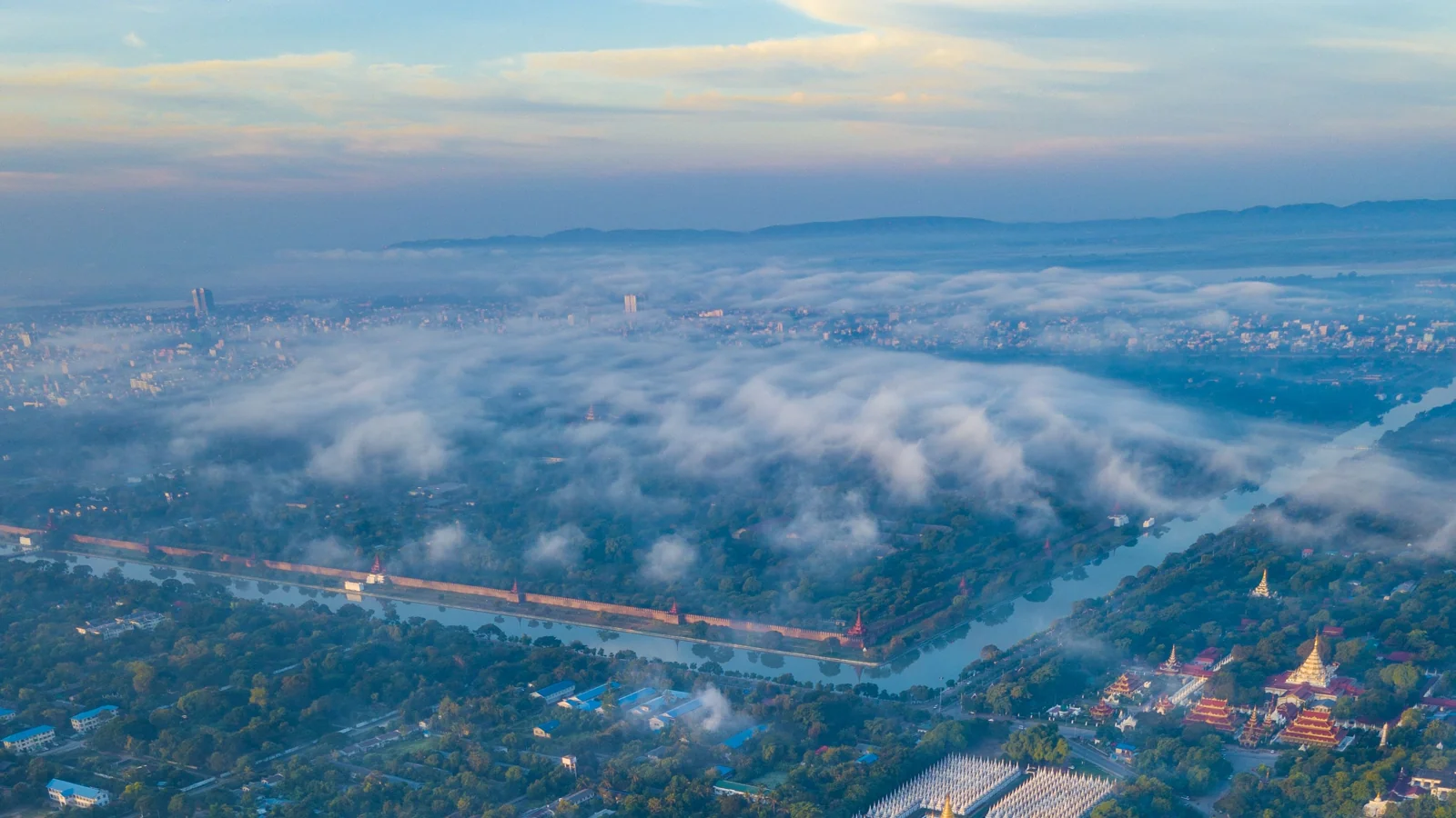 Mandalay’s palace moat and northern cityscape beneath low cloud, photographed from above.