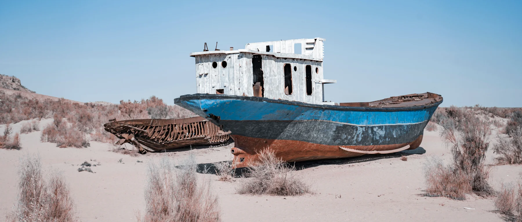 Blue and white abandoned fishing boat beside rusting hulls on the former seabed at Muynak, Uzbekistan