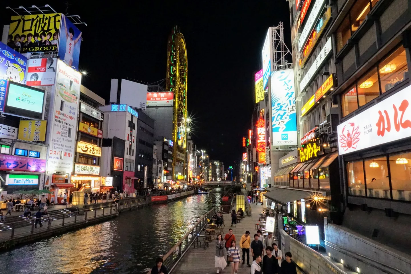 Illuminated Dotonbori canal with signs and the oval riverside Ferris wheel