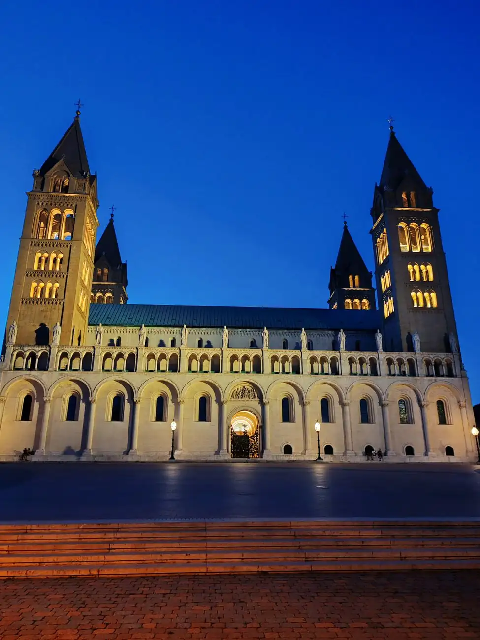 The four illuminated towers and long arcaded façade of Pécs Cathedral at twilight