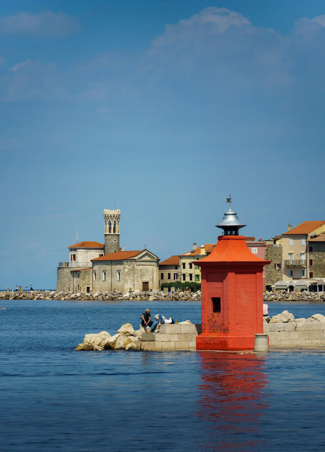 A red harbour beacon with Punta’s church and historic defensive tower beyond in Piran
