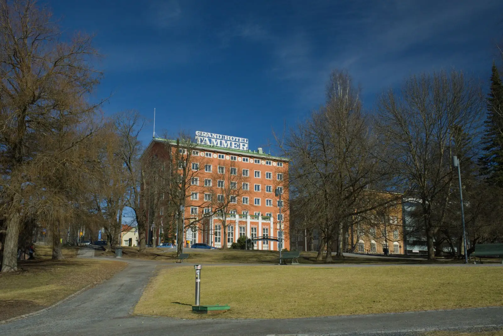 Front view of Grand Hotel Tammer surrounded by trees on a sunny day in Tampere, Finland.