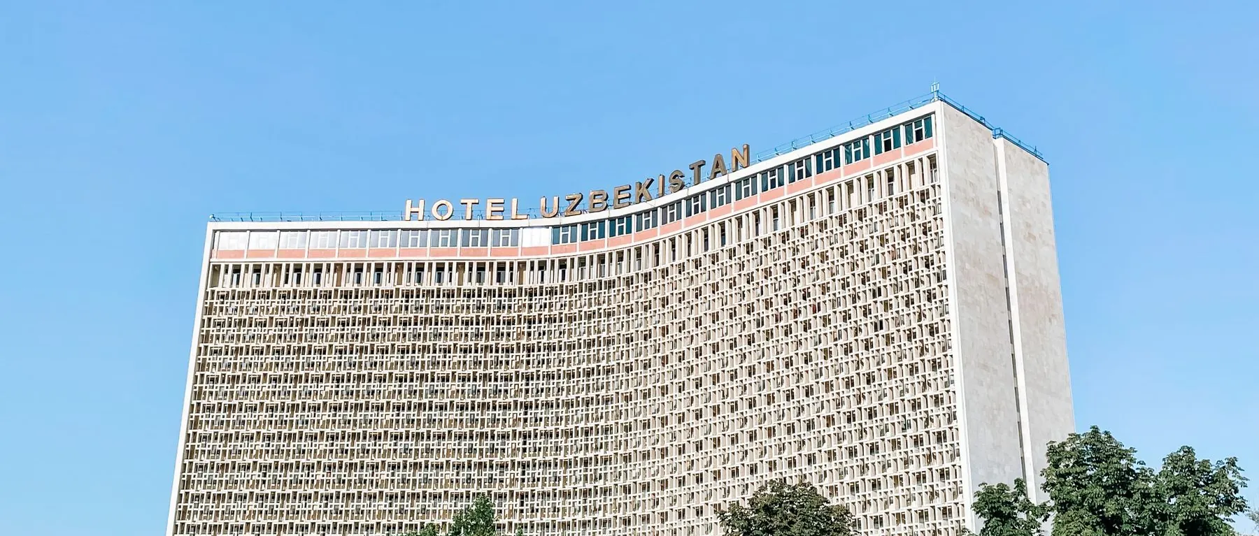 Hotel Uzbekistan’s patterned curved facade beside trees near Amir Temur Square in Tashkent