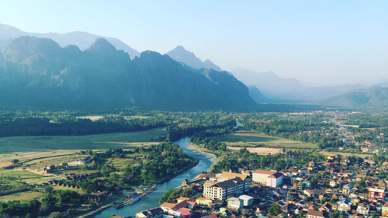 The Nam Song River winding between Vang Vieng’s buildings and a wall of limestone mountains.