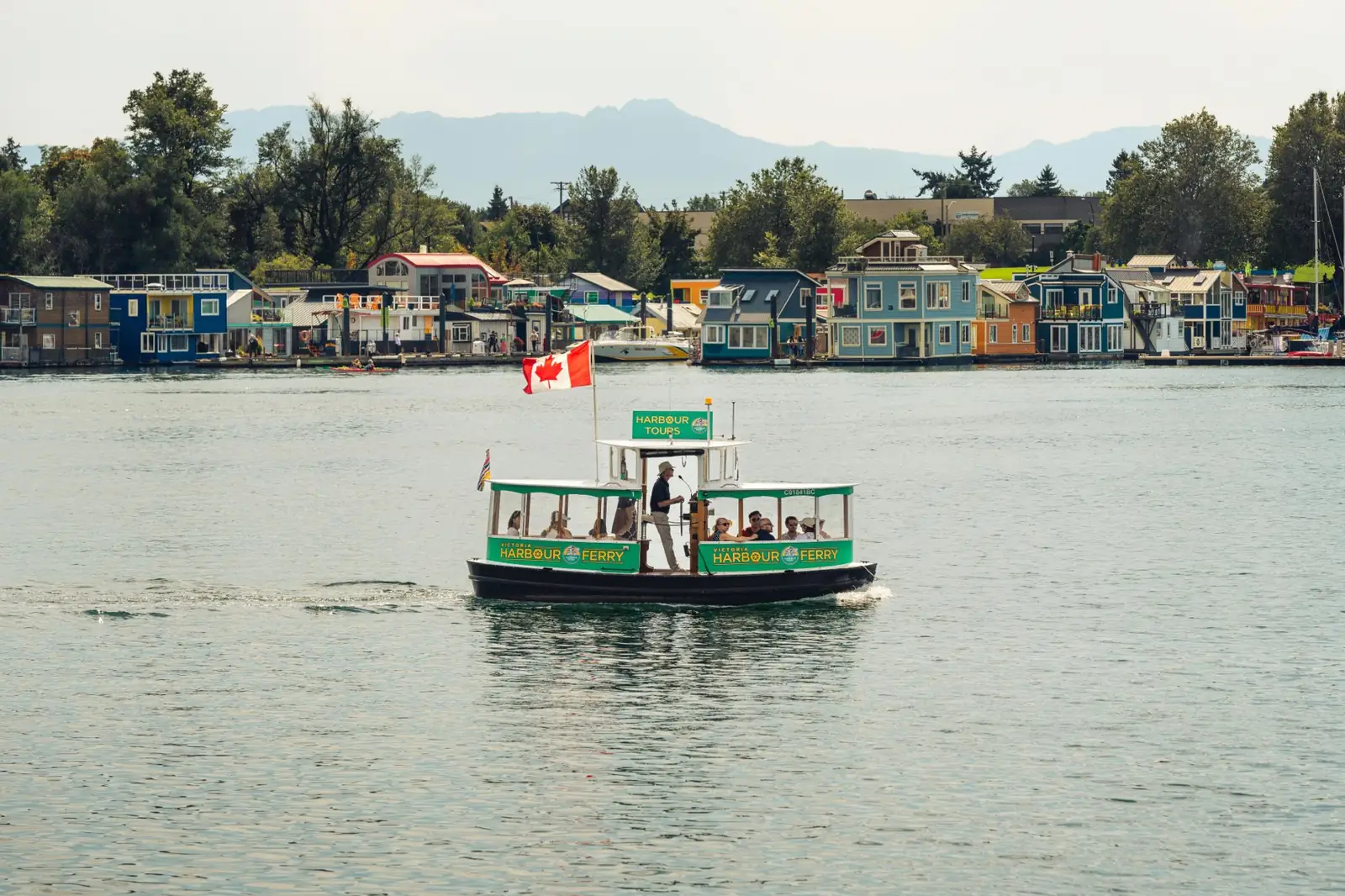 A green Victoria Harbour Ferry boat beside colourful floating homes at Fisherman’s Wharf
