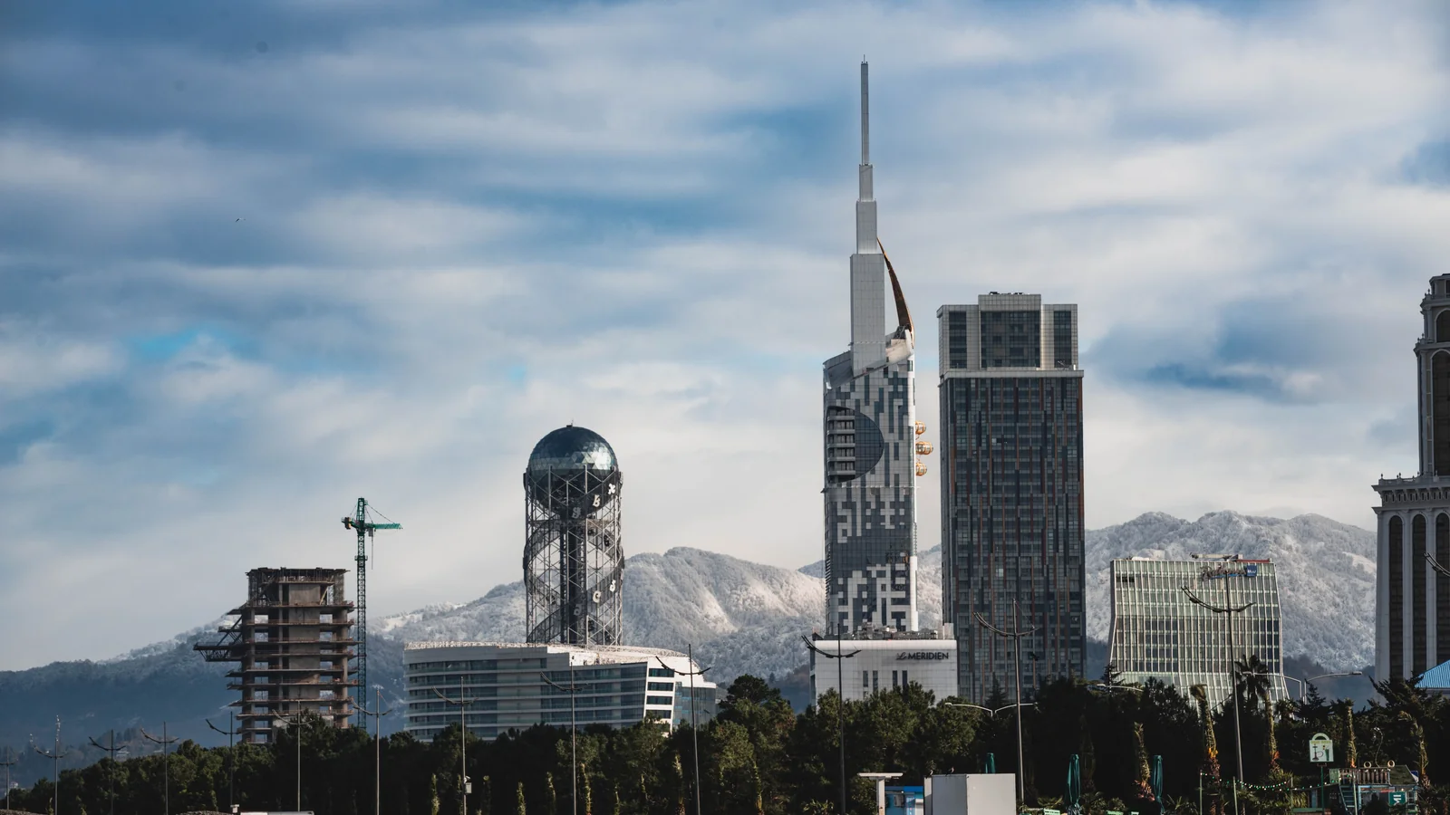 Batumi’s Alphabet Tower and tall modern skyline, with snow-covered mountains behind the Black Sea city.
