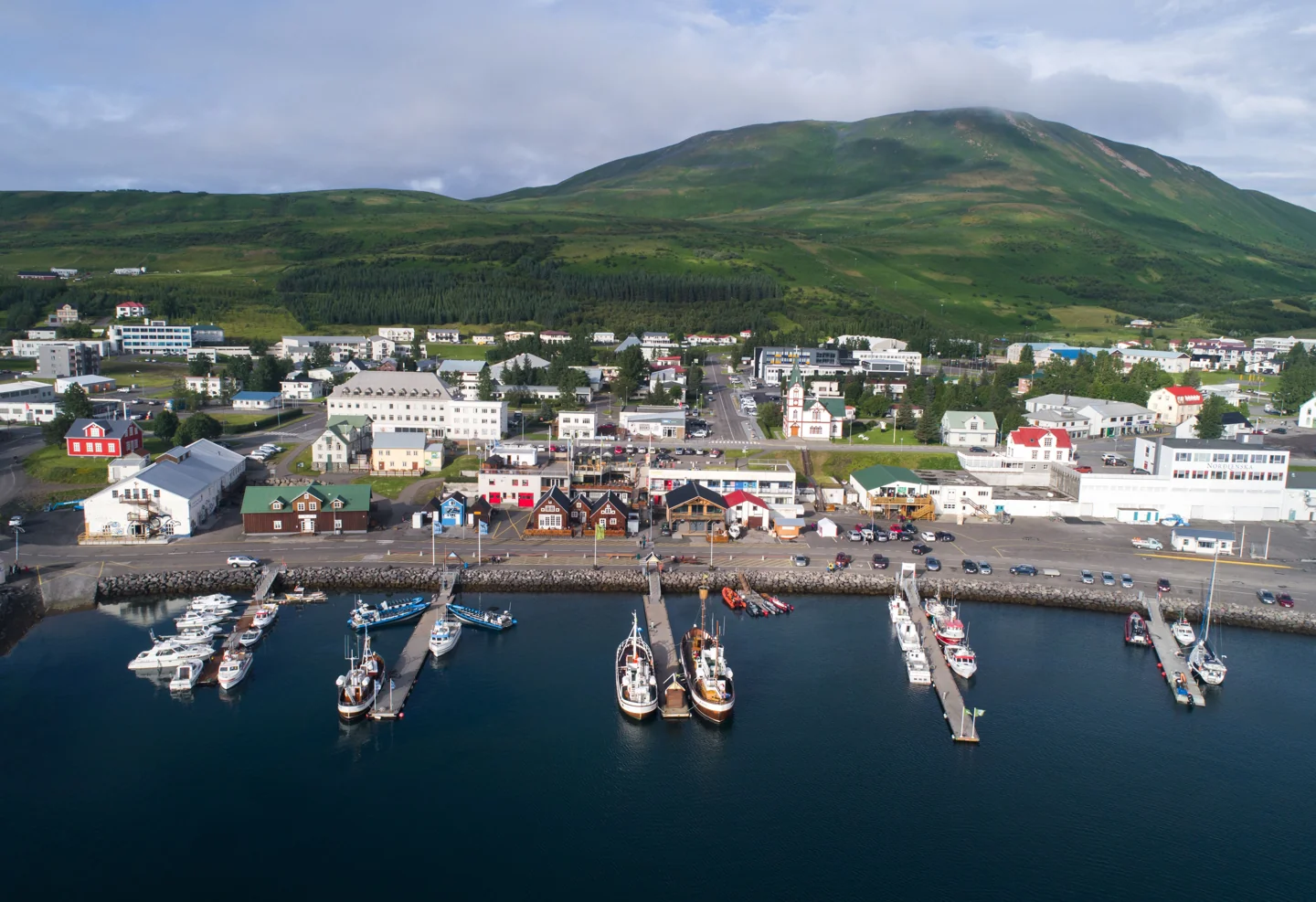 Húsavík harbour, its central buildings and wooden church below a green hillside