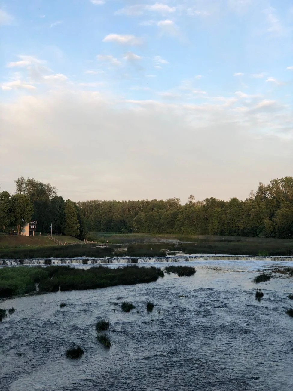 Venta Rapid flowing across the broad river in Kuldīga beneath a wooded bank
