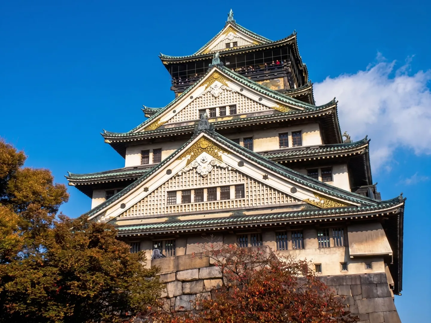 Osaka Castle’s green-roofed main tower above its stone base and autumn trees